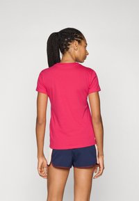 Rosa kortermet T-skjorte laget av glatt bomull, med rund hals og tettsittende design, brukt sammen med mørke shorts.