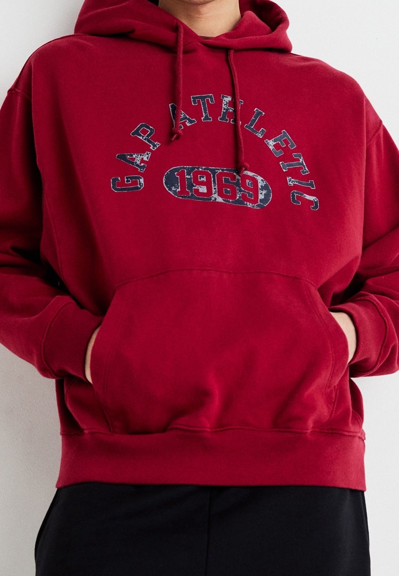 Rode hoodie gemaakt van een katoenmix. Bevat een voorzak, ribgebreide manchetten en een grafische print "GAP ATHLETIC 1969" in het blauw.