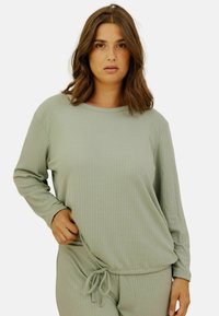 Haut à manches longues côtelé vert clair avec un col rond et un cordon de serrage ajustable à l'ourlet, associé à un pantalon assorti. Texture douce.
