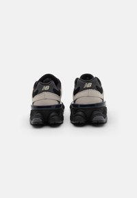 Black and gray sneakers featuring a mesh and suede upper, curved sole, and a glossy accent on the heel with a logo on the back.