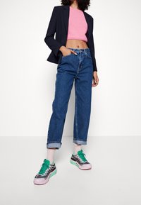 Blå denim jeans med hög midja och uppvikta ben, i kombination med en rosa kortärmad tröja och svarta/gröna sneakers med rosa detaljer.