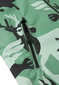 Zielona tkanina w wzory z czarnymi motywami jeleni, z czarnym zamkiem błyskawicznym z przodu. Gładka tekstura, nowoczesny design.