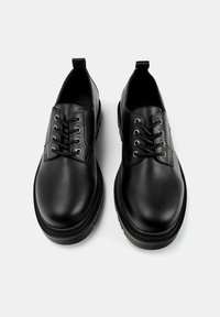 Pantofi din piele neagră cu un finisaj neted, formă rotundă și design cu șireturi. Prezintă gauri metalice pentru șireturi și o talpă din cauciuc texturată pentru aderență.