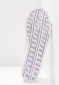 White sneaker with a textured rubber sole, featuring a herringbone pattern. The upper has a smooth, minimalistic design with no visible branding.