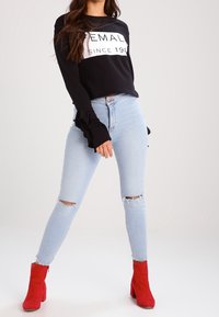 Svart sweatshirt med vit text, volangärmar; ljusblå slitna skinny jeans; röda ankelskoboots med blockklack.