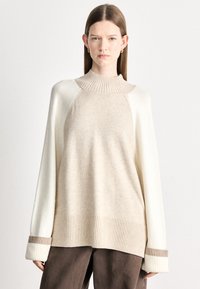 Μπεζ και εκρού πλεκτό πουλόβερ με ψηλό γιακά, ριμπ τελείωμα και φαρδιά μανίκια με καφέ λεπτομέρεια. Μαλακή υφή και άνετη γραμμή.