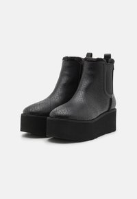 Botines negros de tobillo hechos de material suave, con un diseño texturizado, suela de plataforma y forro de piel sintética en la parte superior.