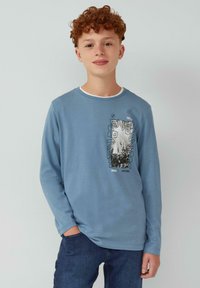Langärmliges blaues Baumwoll-T-Shirt mit rundem Halsausschnitt und einem grafischen Druck auf der Brust, der schwarze Akzente und Text enthält.