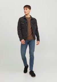 Veste en denim noir sur un pull texturé marron, associée à un jean slim bleu et des chaussures noires, avec un design classique et des poches avant.