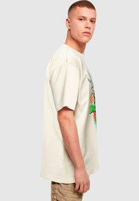 Cremefarvet oversized t-shirt med korte ærmer, der har et farverigt tegneserie-motiv på forsiden og en afslappet pasform.