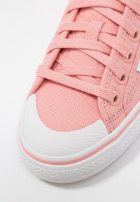 Primo piano di una sneaker di tela rosa con lacci coordinati, punta in gomma bianca e suola bianca testurizzata con una sottile striscia rosa.