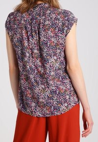 Blusa floral en azul oscuro con mangas cortas, que presenta un estampado de flores dispersas en varios colores y un diseño de espalda plisada.