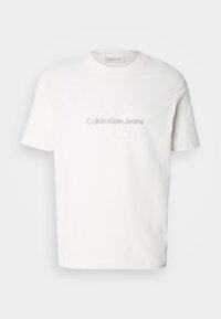 Bílá bavlněná tričko s kulatým výstřihem a krátkými rukávy, s vyšitým logem "Calvin Klein Jeans" v světle šedé barvě na hrudi.