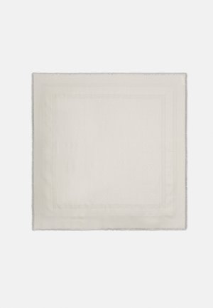 Serviette carrée en tissu de couleur crème avec une bordure subtilement texturée et des bords légèrement effilochés sur un fond uni.