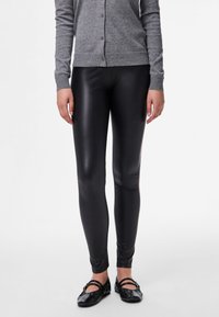 Black, high-shine leggings with a slim fit, made of stretchy material, paired with a gray button-up cardigan and black ballet flats.