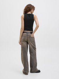 Top senza maniche nero abbinato a jeans in denim beige chiaro, larghi e a gamba larga, con due tasche posteriori e dettagli di cuciture visibili.