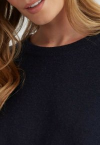 Maglione blu scuro con scollatura rotonda, texture morbida e lavorazione fine. Capelli che incorniciano il viso creano un aspetto naturale.