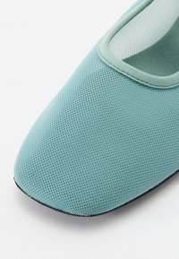 Ljus teal platt sko med ovandel av mesh, rund tå och mjuka kanter. Texturerad yta med en slät svart sula.