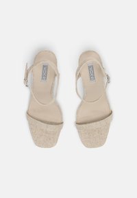 Beige plateau sandalen met gestructureerde stoffen banden, open teen ontwerp en enkelbandjes. De buitenzool is plat en glad.