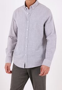 Ljusgrå skjorta med knappar och en subtil textur, långa ärmar och en knapp-ner krage. Framsidan har vita knappar.