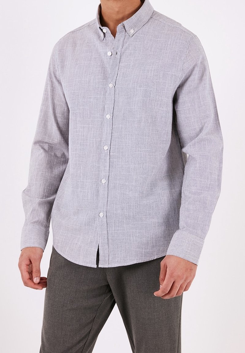 Ljusgrå skjorta med knappar och en subtil textur, långa ärmar och en knapp-ner krage. Framsidan har vita knappar.