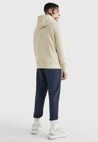 Felpa beige con vestibilità comoda e cappuccio regolabile, abbinata a pantaloni della tuta blu navy. Scarpe da ginnastica bianche e calzini bianchi strutturati completano l'outfit.