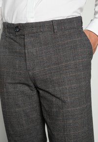 Grijze geruite broek van een gestructureerde stof. Voorzien van een knoopsluiting, zijzakken en een getailleerde pasvorm met subtiele ruitpatronen in donkerdere tinten.