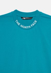 Camiseta de algodón color teal con cuello redondo acanalado que presenta el logo "THE NORTH FACE" en blanco. Textura suave, diseño casual, mangas cortas.
