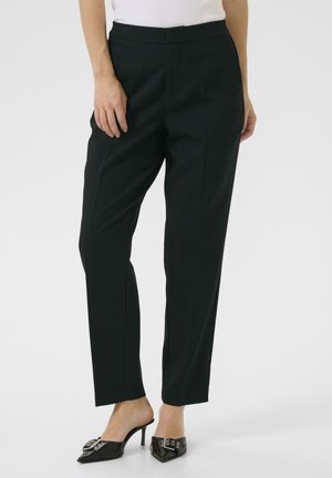 Pantalon noir ajusté avec une coupe droite, texture lisse et taille mi-haute. Associé à des mules à talons noirs brillantes.