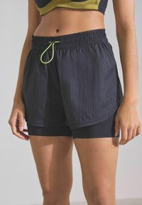 Naiste mustad spordishortsid, mis on valmistatud kerge kangaga, omavad elastset vöökohta koos särava rohelise paelaga ja sisseehitatud voodriga.