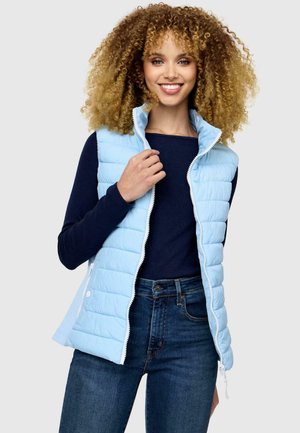 Hellblau gepolsterte Weste mit hohem Kragen und Vorderreißverschluss, kombiniert mit einem navyblauen Langarmoberteil und dunklen Jeans.