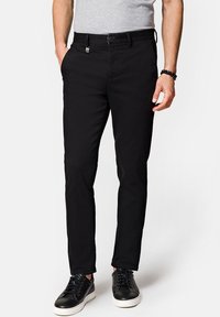 Czarne bawełniane spodnie o wąskim kroju, z paskiem na paski i zamkiem błyskawicznym. Posiada boczne kieszenie i gładką fakturę. Noszone z czarnymi trampkami.