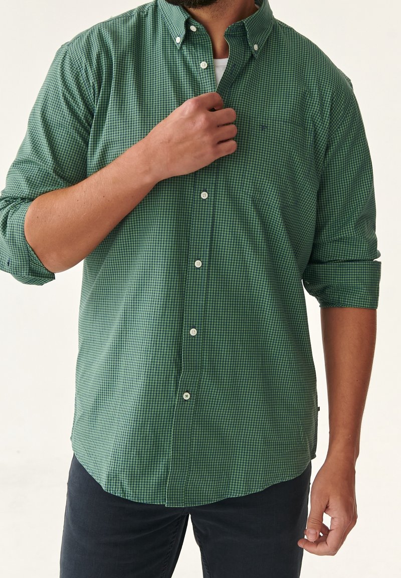 Camisa de cuadros verdes de botones, hecha de tela de algodón, con un cuello clásico y mangas enrolladas, que cuenta con botones blancos y un bolsillo en el pecho.