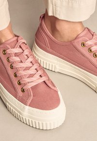 Rausvos drobinės sportbačiai su kontrastinga balta guminė puse, metalinėmis akutėmis ir raštuotomis raištelėmis, žemomis batų lankstymo dalimis ir tekstūruota medžiaga.