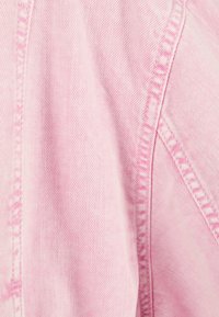 Rosa denimtyg med synlig diagonal väv och sydda sömmar i närbild.