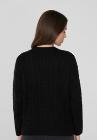 Schwarzer Kabelstrickpullover mit rundem Halsauschnitt und langen Ärmeln, der ein strukturiertes Muster auf der Rückseite zeigt.