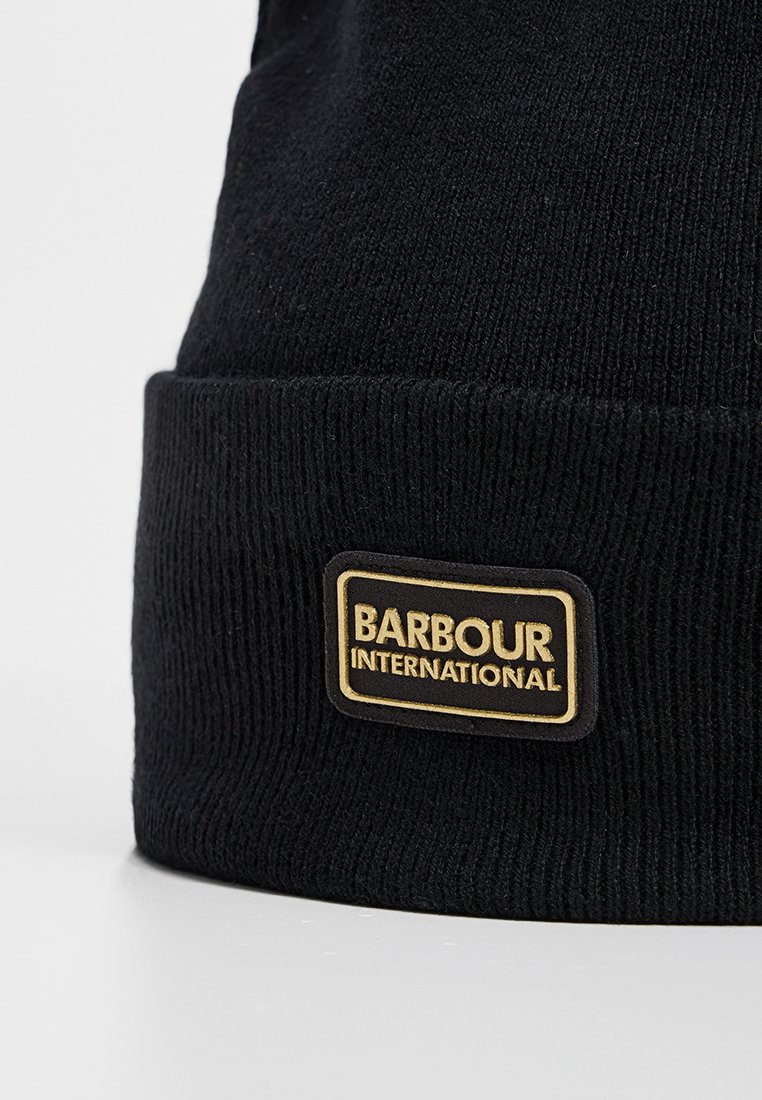 Czarna czapka dzianinowa z prążkowaną strukturą i podwiniętym mankietem. Zawiera prostokątną złoto-czarną metkę z logo "BARBOUR INTERNATIONAL".