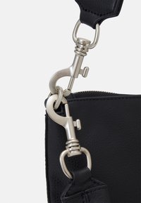 Dettaglio di una borsa in pelle nera con una chiusura metallica e componenti di attacco, che mostra una finitura testurizzata e una costruzione robusta.