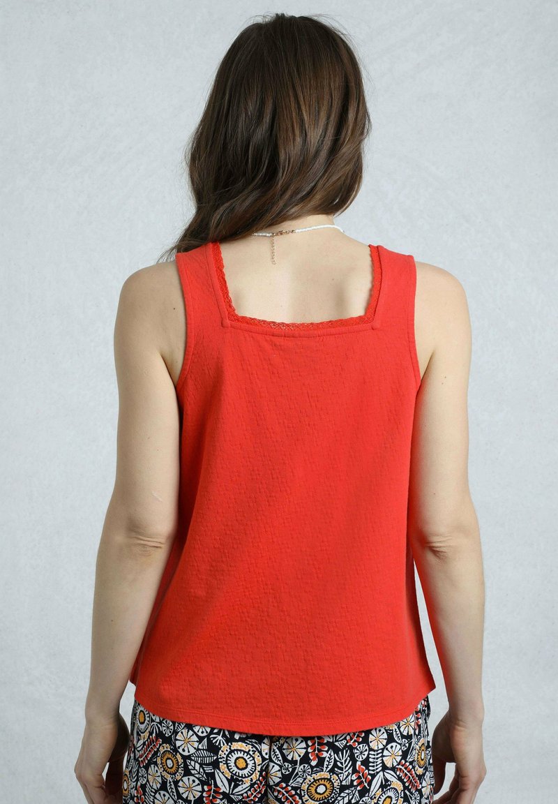 Red tank top with a square neckline, textured fabric, and decorative lace trim at the edges, paired with patterned black and white pants.