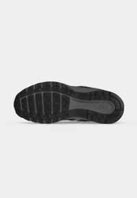 Σόλα από μαύρο και γκρι αθλητικό παπούτσι Nike που δείχνει λεπτομερή μοτίβο πέλματος και το λογότυπο Nike σε ανοιχτό γκρι φόντο.