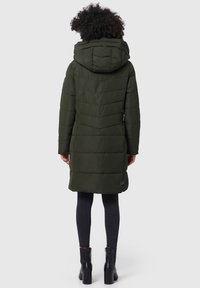 Groene gewatteerde jas met een capuchon, voorzien van horizontale en chevronstiksels. Het ontwerp reikt tot halverwege de dijen, gecombineerd met strakke zwarte jeans en laarzen.