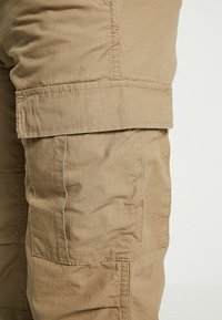Beiget väriset cargo-housut, jotka on valmistettu kevyestä kankaasta. Niissä on teksturoitu pinta, sivutaskut ja kestävyyttä lisäävä vahvistettu ommel.