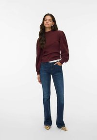 Un pull bordeaux à manches bouffantes, associé à un jean bleu évasé et des talons aiguilles en imprimé serpent. Design simple, texture douce.