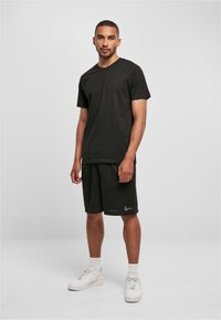 T-shirt en coton noir et shorts noirs, tous deux de coupe décontractée. Baskets blanches avec des semelles texturées, assorties de chaussettes blanches.