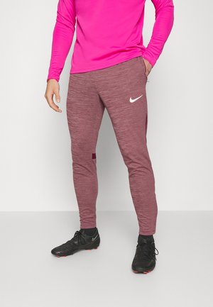 Bordowe spodnie sportowe o teksturowanym wykończeniu i bocznymi kieszeniami, zestawione z żywym różowym T-shirtem z długim rękawem oraz czarnymi butami.