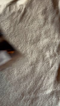 Tissu en feutre de couleur blanc cassé avec une surface douce et texturée. Bord d'une forme triangulaire foncée partiellement visible, indiquant un objet possible.