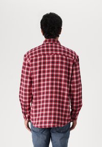 Koszula w kratę w czerwono-czarno-białe wzory, z długimi rękawami, prostym kołnierzykiem i zapinanym na guziki karczkiem z tyłu; materiał bawełniany.