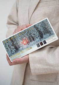 Persona sosteniendo una caja de velas aromáticas Skandinavisk Winter Solstice con un diseño de bosque invernal y atardecer en el embalaje.
