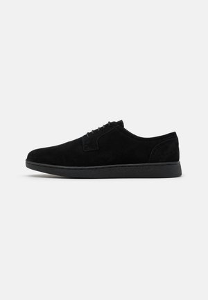 Black suede lace-up shoes with a sleek design, rounded toe, and a textured black rubber sole. Simple stitching along the upper.