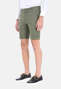 Pantaloni corti verde oliva realizzati in tessuto leggero, con taglio dritto, orli ripiegati e tasche laterali, abbinati a scarpe nere.